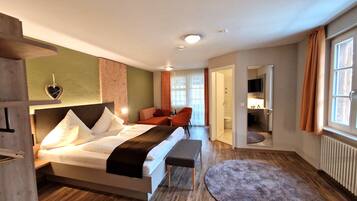 A hotel room with a bed, a bench, a small table, and a bathroom visible through an open door.