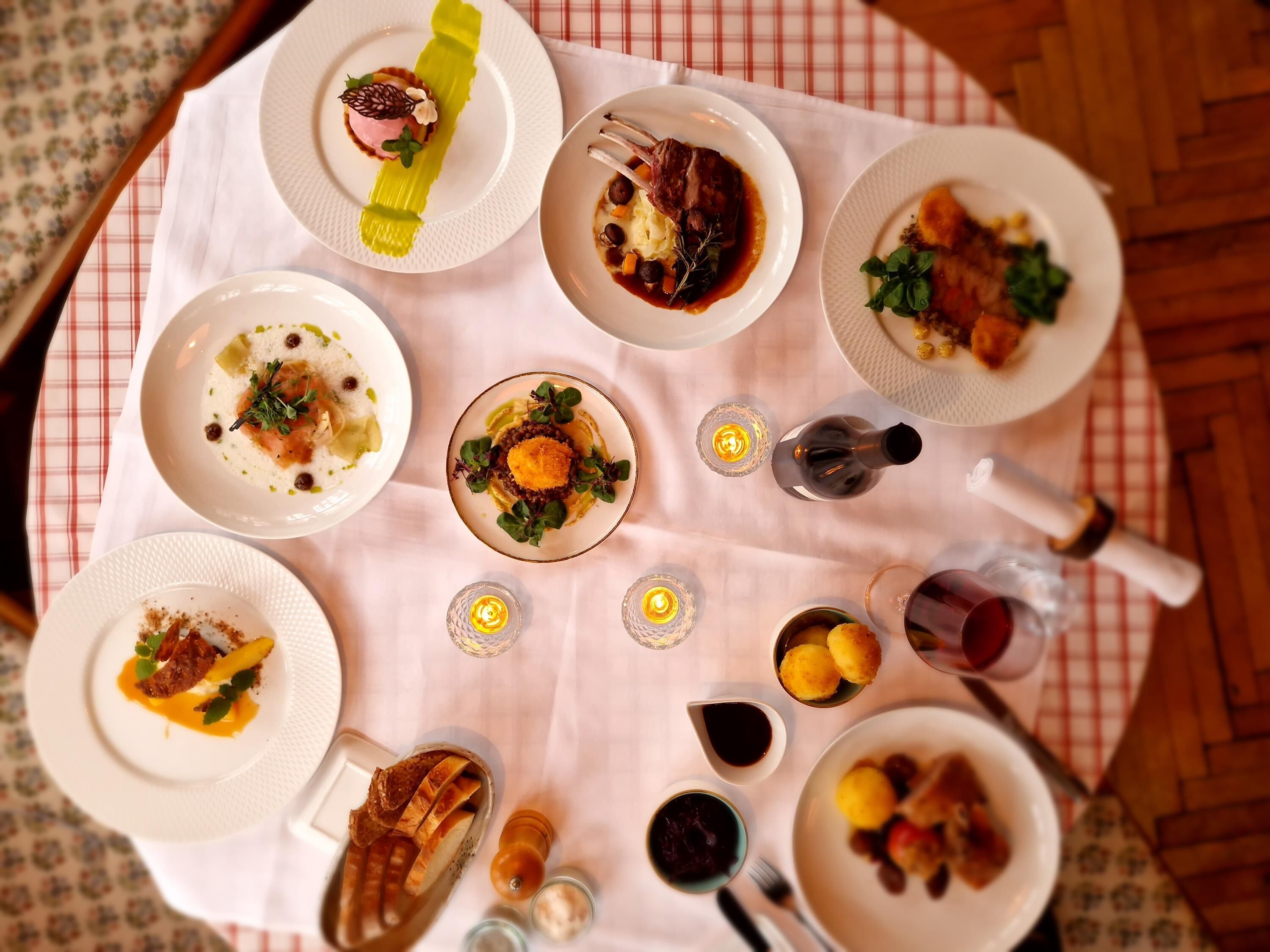 Una mesa de comedor con diferentes platos, velas y una botella de vino.