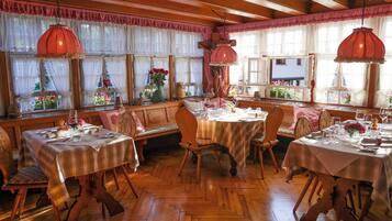 Zona pranzo con tavoli e sedie in legno, ampie finestre con tende e lampade rosse pendenti.