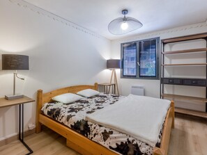 A bedroom with a wooden bed, a desk with a lamp, a chair, a radiator, and a window with blinds. - 3-room apartment, terrace, pets allowed, garage, village center (La Clusaz)