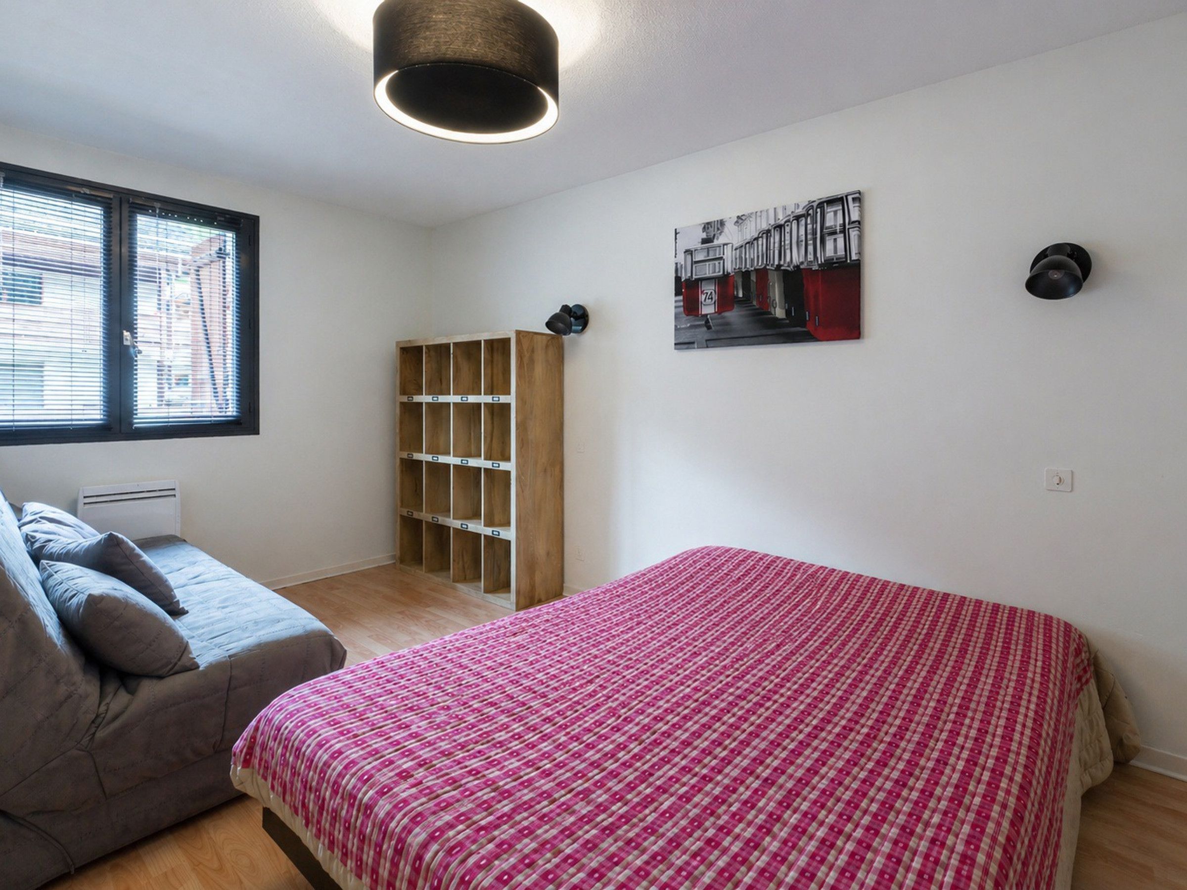 A bedroom with a bed, a sofa, a built-in wardrobe, a ceiling light, and a wall-mounted picture.