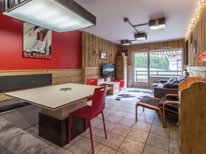 Ein Essbereich mit Tisch und Stühlen, einem Fernseher und einer Couch in einem Raum mit Holzwänden und Fliesenboden.