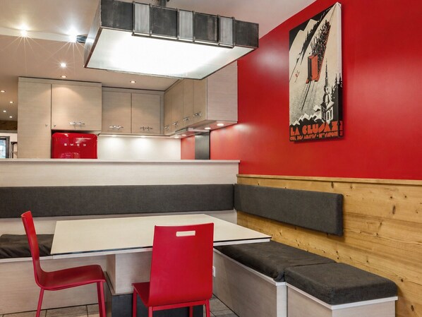 A modern dining area with a white table, red chairs, and a bench.