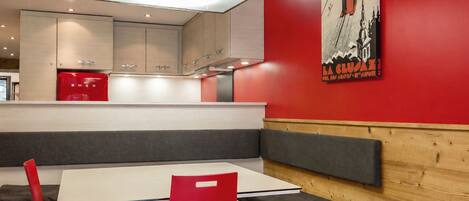 A modern dining area with a white table, red chairs, and a bench.
