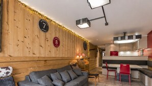 A cozy living area with a sofa, chairs, a dining table, and a kitchen in the background. - 3-room apartment, terrace, pets allowed, garage, village center (La Clusaz)