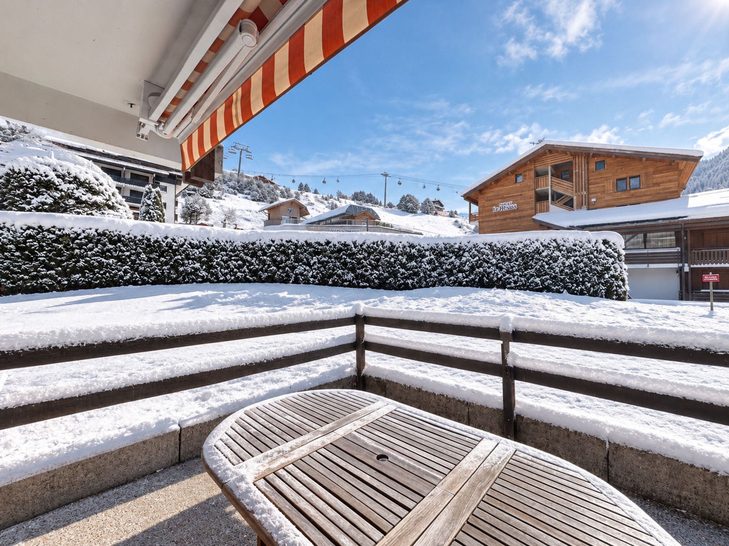 A snow-covered outdoor seating area with a wooden table and steps leading to a building with a sign.