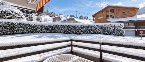 A snow-covered outdoor seating area with a wooden table and steps leading to a building with a sign.