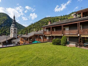 A traditional wooden building with a balcony, a bell tower, and a green lawn in front.