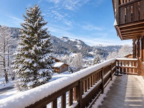 Un balcón de madera con barandilla cubierta de nieve que da a un paisaje montañoso con casas.