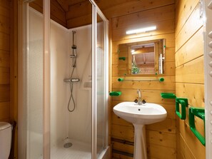 A wooden-paneled bathroom with a glass-enclosed shower, a pedestal sink, and a mirror above the sink.