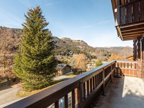 Een houten balkon met uitzicht op een bergachtig landschap en een kleine blokhut.