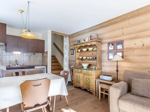 A cozy interior with a wooden dining table, chairs, a sofa, a cabinet with dishes, and a staircase leading to another room.