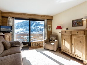 A cozy living room with a large window, a television, a red lamp, and a wooden cabinet.