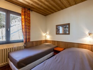 Quarto com duas camas, janela com vista para uma paisagem nevada, colagem de fotografias na parede e radiador.
