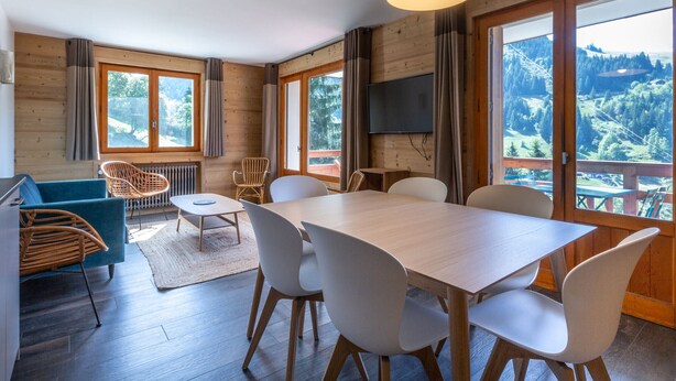A modern room with a dining table, chairs, a sofa, and a TV.
