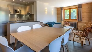 A modern kitchen with a microwave and stove, a dining area with a wooden table and white chairs, and a window with a view of trees.