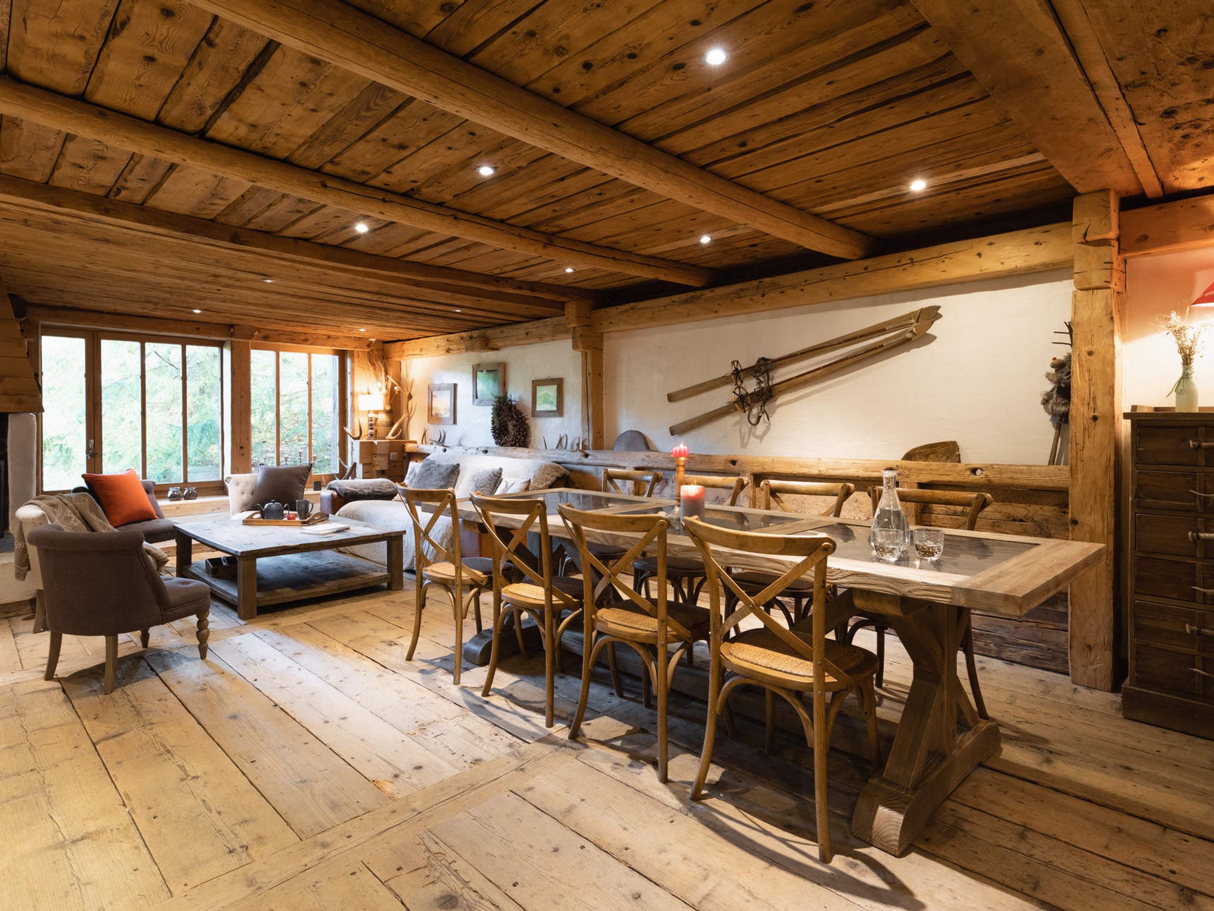 A rustic interior with wooden beams, a dining table with chairs, a sofa, and a fireplace.
