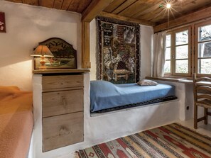 Une pièce confortable avec un lit intégré, une commode en bois, une tapisserie et une fenêtre donnant sur un beau paysage.