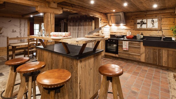 Una cocina rústica con vigas de madera, una isla central, taburetes, una estufa y un fregadero.