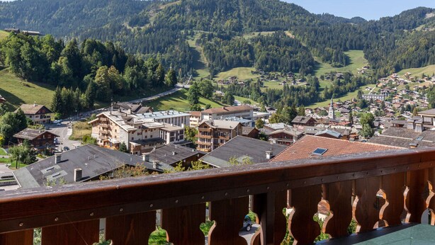 A town with traditional architecture, a river, and surrounding hills.