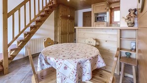 A wooden interior with a staircase, a dining table, a kitchen area, and a microwave.