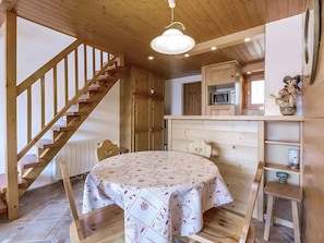 A wooden interior with a staircase, a dining table, a kitchen area, and a microwave.