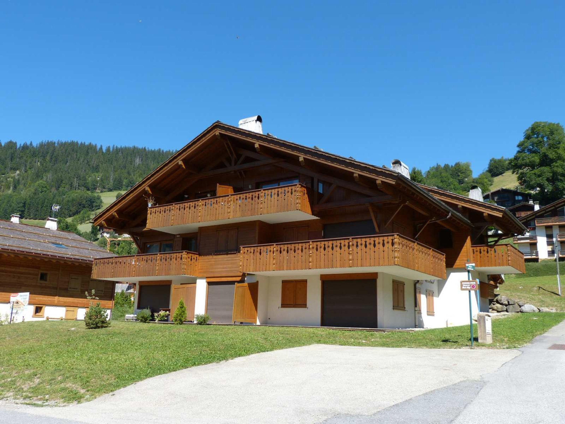 A two-story wooden chalet with balconies, a garage, and a view of a forested hillside.