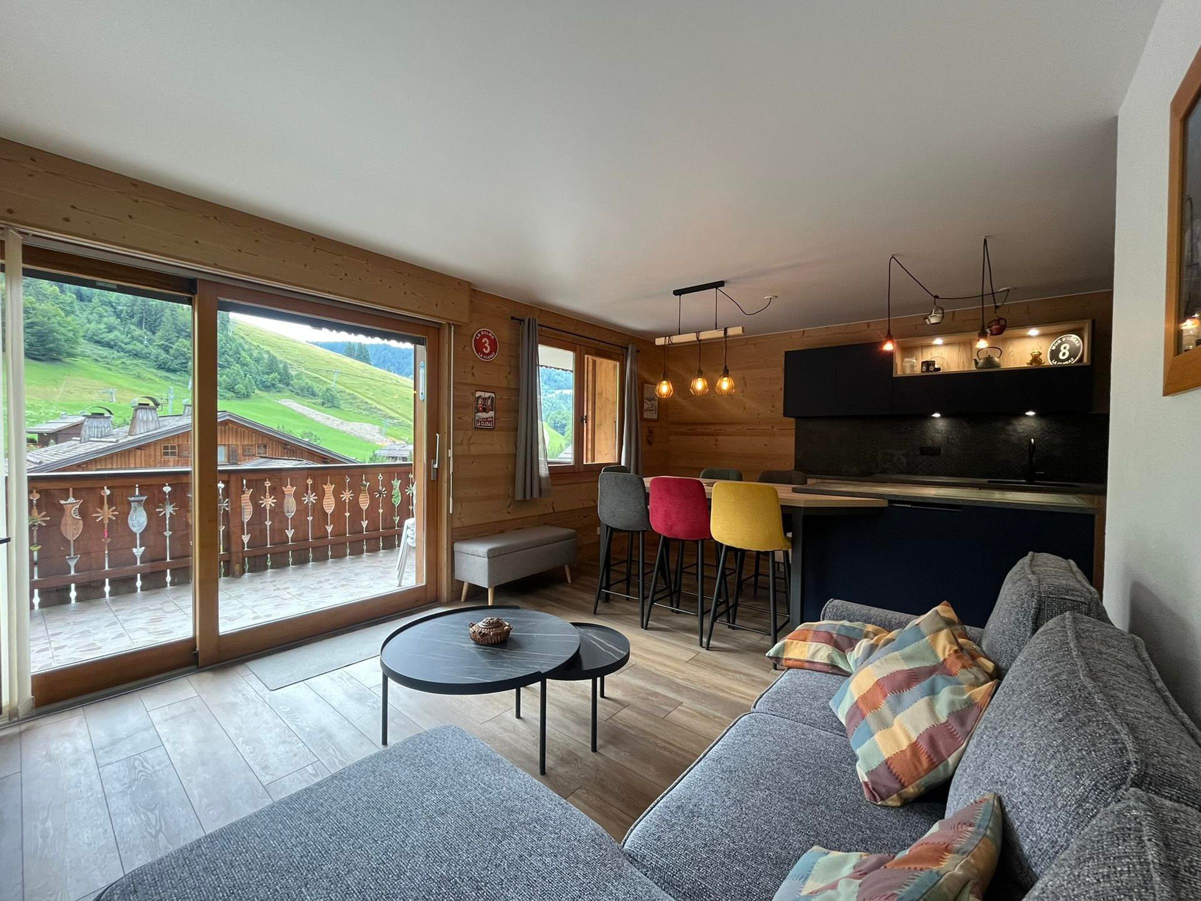 Un intérieur moderne avec un plancher en bois, un canapé, une table ronde et un coin bar avec des tabourets.