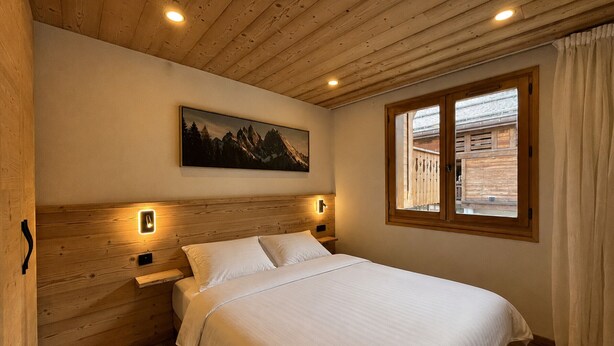 Une chambre avec un plafond en bois, un lit avec une literie blanche, un tableau au mur et une fenêtre avec des rideaux.