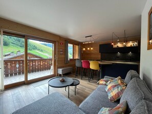A modern interior with a wooden floor, a sofa, a round table, and a bar area with stools.