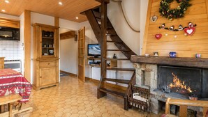 Een knus interieur met een houten trap, een open haard en een keukenhoek.