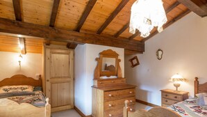 Een slaapkamer met twee houten bedden, een dressoir met lades, een spiegel en een nachtkastje met een lamp.