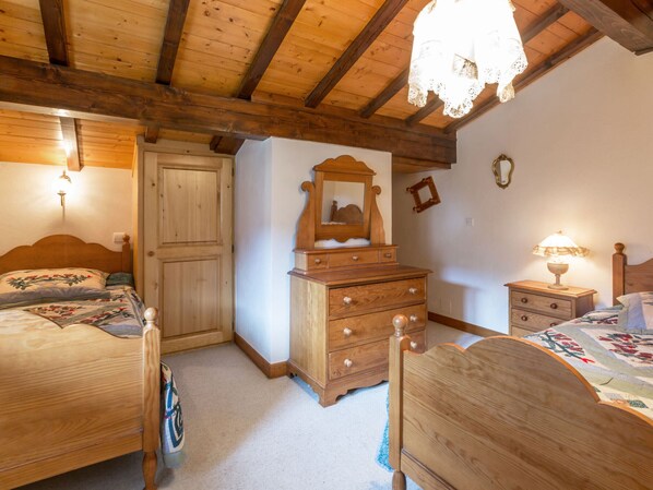 Un dormitorio con dos camas de madera, un aparador con cajones, un espejo y una mesita de noche con lámpara.