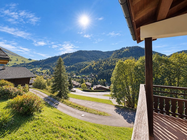 A mountainous landscape with a clear sky, a wooden building with a balcony, and a road leading through the valley.
