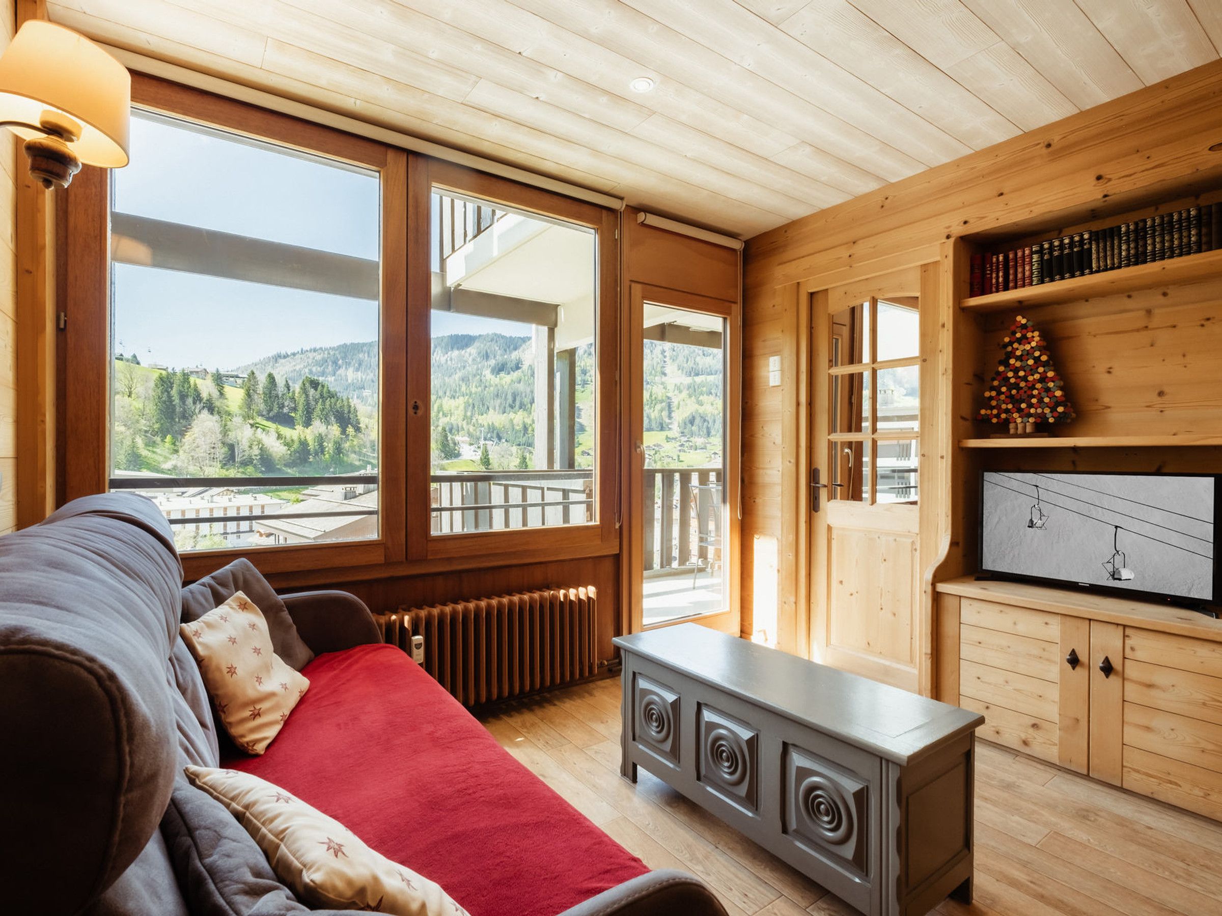 A cozy room with a large window, a wooden cabinet, and a red blanket on a sofa.