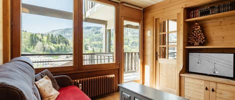 A cozy room with a large window, a wooden cabinet, and a red blanket on a sofa.