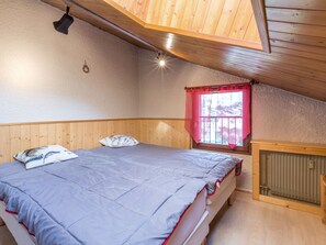 A bedroom with a bed, wooden walls, a window with a red curtain, and a radiator. - 3*** Studio by slopes, fireplace, pets allowed, garage (La Clusaz)