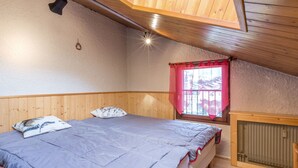 A bedroom with a bed, wooden walls, a window with a red curtain, and a radiator. - 3*** Studio by slopes, fireplace, pets allowed, garage (La Clusaz)