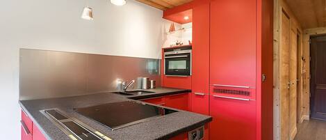 A modern kitchen with a red island, stainless steel appliances, and pendant lighting.