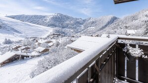 A snowy mountain village with buildings and trees covered in snow, a clear sky, and a wooden balcony railing. - Spacious apt 7 ppl, 3*, quiet, La Clusaz (La Clusaz)