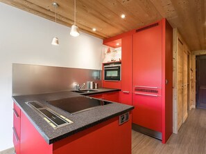 A modern kitchen with a red island, stainless steel appliances, and pendant lighting.