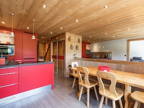 A modern kitchen with wooden cabinets, a red island, and a dining area with wooden chairs and a table.