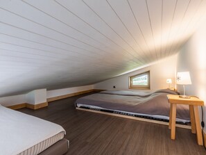 A bedroom with a sloped ceiling, a bed, a bedside table with a lamp, and a window.