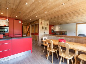 A modern kitchen with wooden cabinets, a red island, and a dining area with wooden chairs and a table. - Spacious apt 7 ppl, 3*, quiet, La Clusaz (La Clusaz)