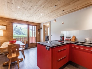 Eine moderne Küche mit roten Schränken, einem Essbereich aus Holz und Blick auf eine grüne Landschaft durch große Fenster.