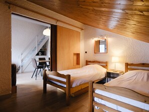 A cozy room with two wooden beds, a small desk, and a chair. A staircase leads to an upper level.