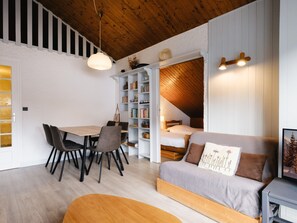 A cozy room with a wooden ceiling, a dining area with chairs and a table, a bookshelf, a bed, and a sofa. - Charming studio near slopes, pets allowed (La Clusaz)
