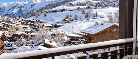 A snow-covered mountain village with wooden buildings, a ski lift, and a view of the mountains.