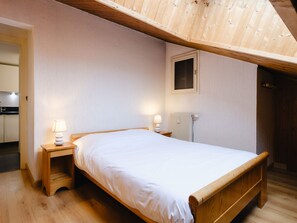 Uma cama de solteiro num quarto com teto inclinado, janela e radiador.