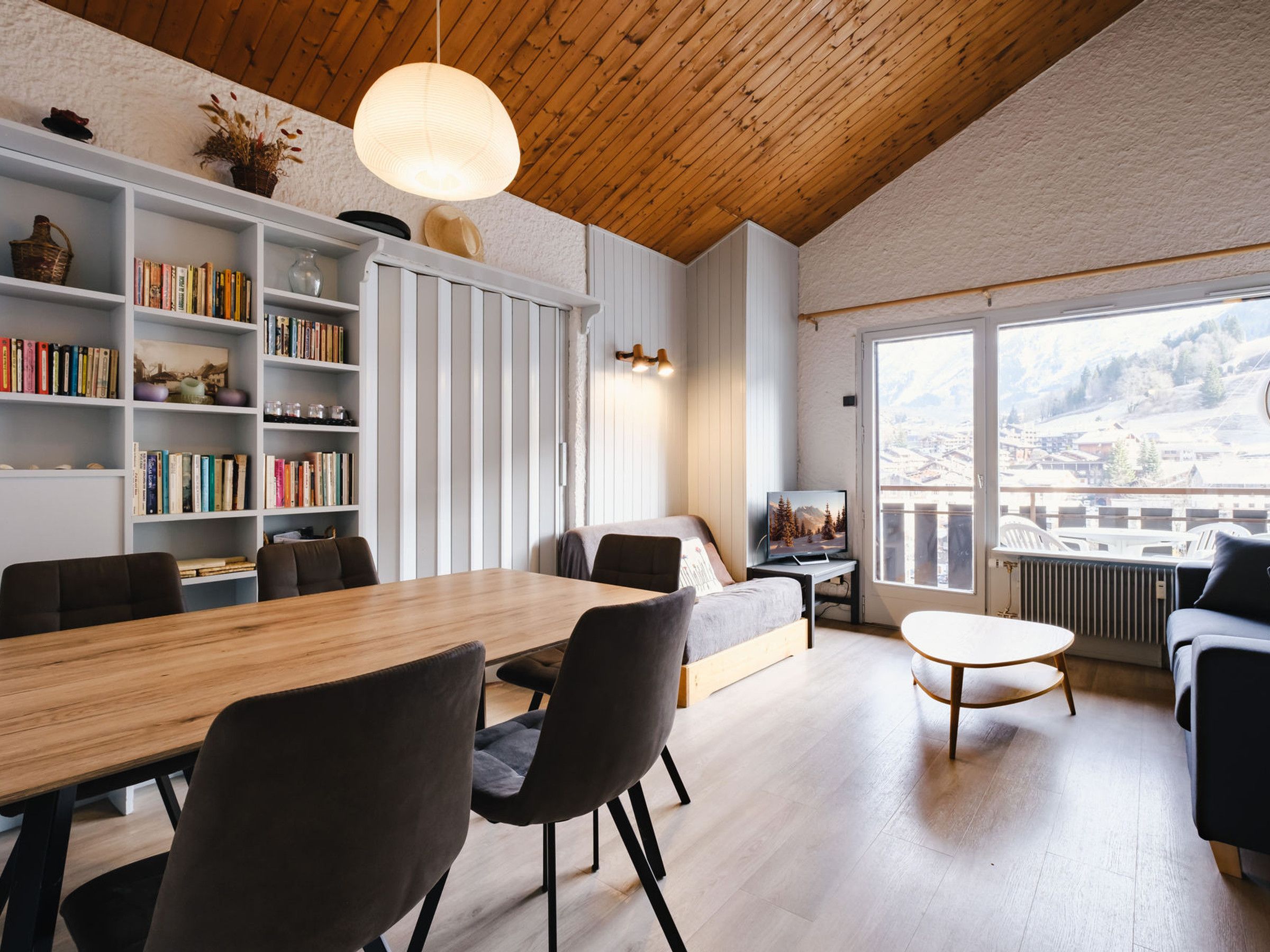 Een moderne woonkamer met een houten plafond, een eethoek en een groot raam met uitzicht op de bergen.